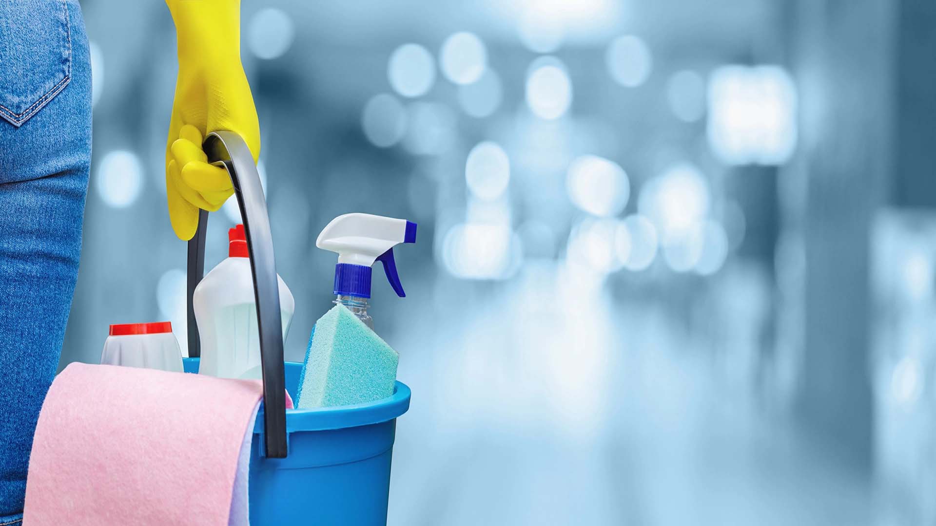 The concept of cleaning service. A cleaning lady is holding a bucket of cleaning products on a blurred background.